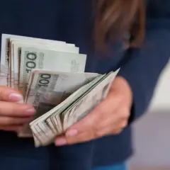 Ręce trzymające plik banknotów 100 zł. Może to być część darowizny domu od rodziców.