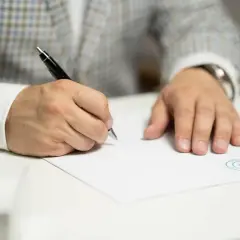 Mężczyzna w eleganckim garniturze podpisuje dokument, który może dotyczyć opłaty za wykreślenie hipoteki z księgi wieczystej.