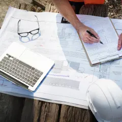 Na budowie trwa analiza dokumentacji. Inżynierowie pracują nad ekspertyzą, analizując plany, notując uwagi i korzystając z laptopa.