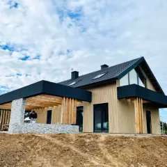 Nowy dom w stanie deweloperskim, z drewnianą elewacją i kamiennym cokołem, czeka na wykończenie.