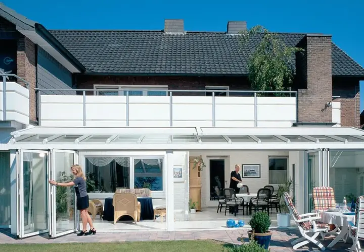 Nowoczesny balkon dostawny do domu jednorodzinnego, z przeszklonym ogrodem zimowym i składanymi drzwiami.