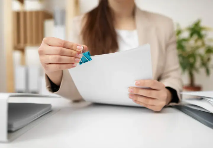 Kobieta z paznokciami ozdobionymi serduszkami trzyma dokumenty, przygotowując się do złożenia wypowiedzenia umowy najmu.