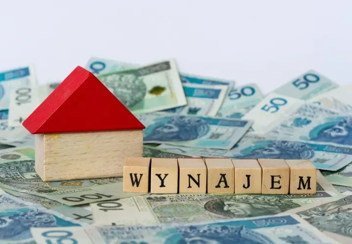 Drewniany domek i kostki z napisem "WYNAJEM" na tle polskich banknotów. Zgłoszenie umowy najmu do urzędu skarbowego.
