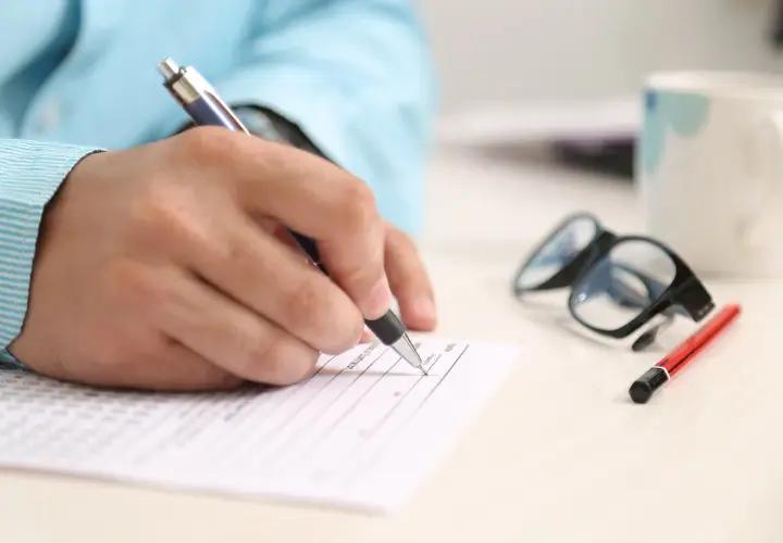 Dłoń pisze na formularzu, obok okulary i kubek. Zastanawiasz się, na co zwrócić uwagę przy kredycie hipotecznym?