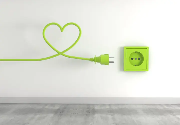 Zielony kabel w kształcie serca podłączony do gniazdka, symbolizujący troskę o niskie opłaty za media.