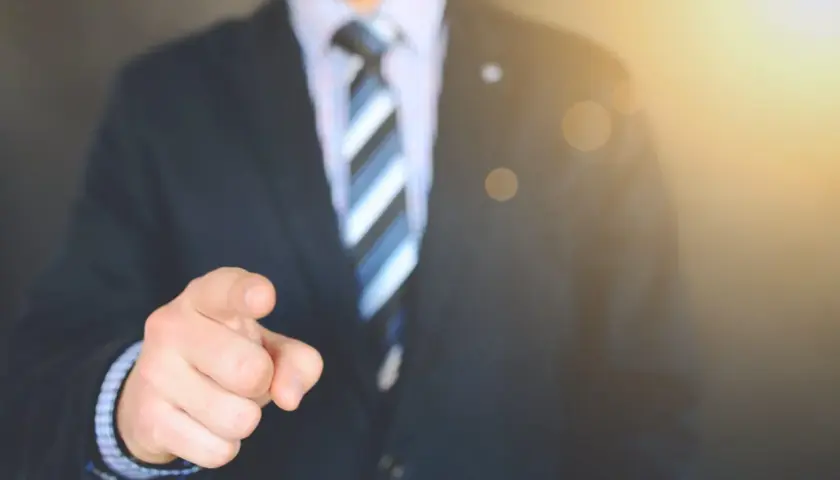 Mężczyzna w garniturze wskazuje palcem, sugerując, jak sprawdzić, kto jest właścicielem mieszkania.