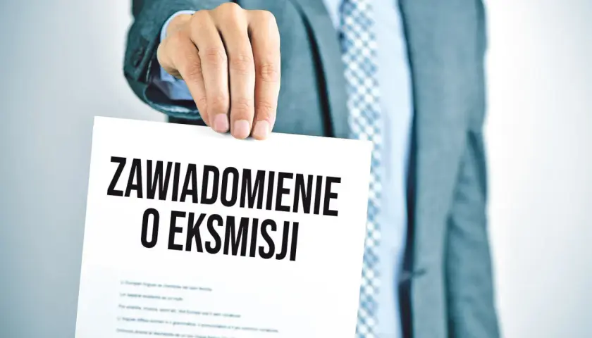 Mężczyzna w garniturze trzyma dokument z napisem "Zawiadomienie o eksmisji", sugerujący wstrzymanie eksmisji z mieszkania.