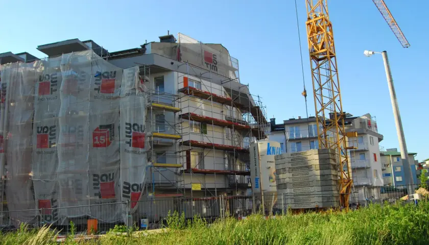 Budowa bloku mieszkalnego z dźwigiem i rusztowaniami.