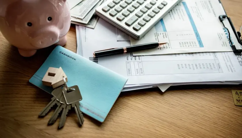 Klucze do domu, świnka-skarbonka, kalkulator i rachunki sugerują planowanie finansowe, w tym waloryzację czynszu najmu.