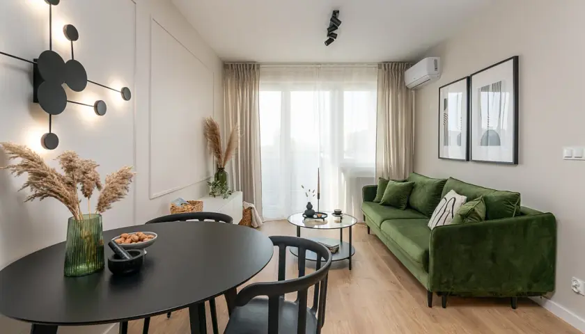 Nowoczesne mieszkanie w bloku z zieloną kanapą, czarnym stołem i designerską lampą.