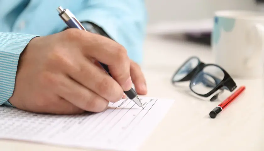 Dłoń pisze na formularzu, obok okulary i kubek. Zastanawiasz się, na co zwrócić uwagę przy kredycie hipotecznym?