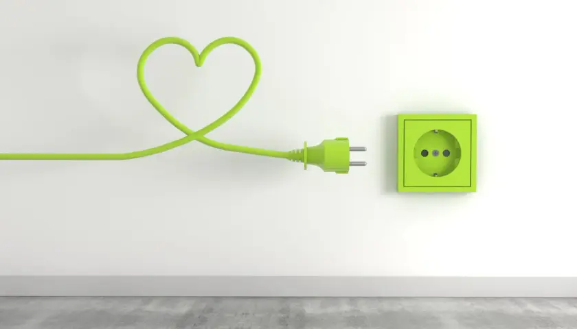 Zielony kabel w kształcie serca podłączony do gniazdka, symbolizujący troskę o niskie opłaty za media.