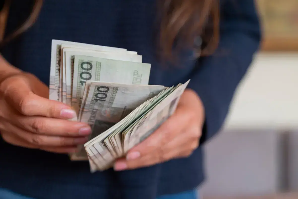 Ręce trzymające plik banknotów 100 zł. Może to być część darowizny domu od rodziców.