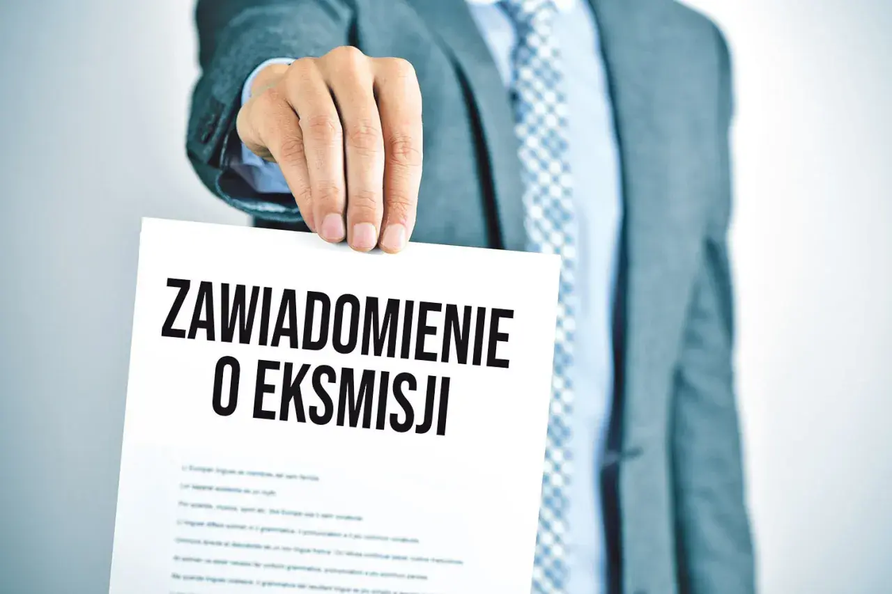 Mężczyzna w garniturze trzyma dokument z napisem "Zawiadomienie o eksmisji", sugerujący wstrzymanie eksmisji z mieszkania.