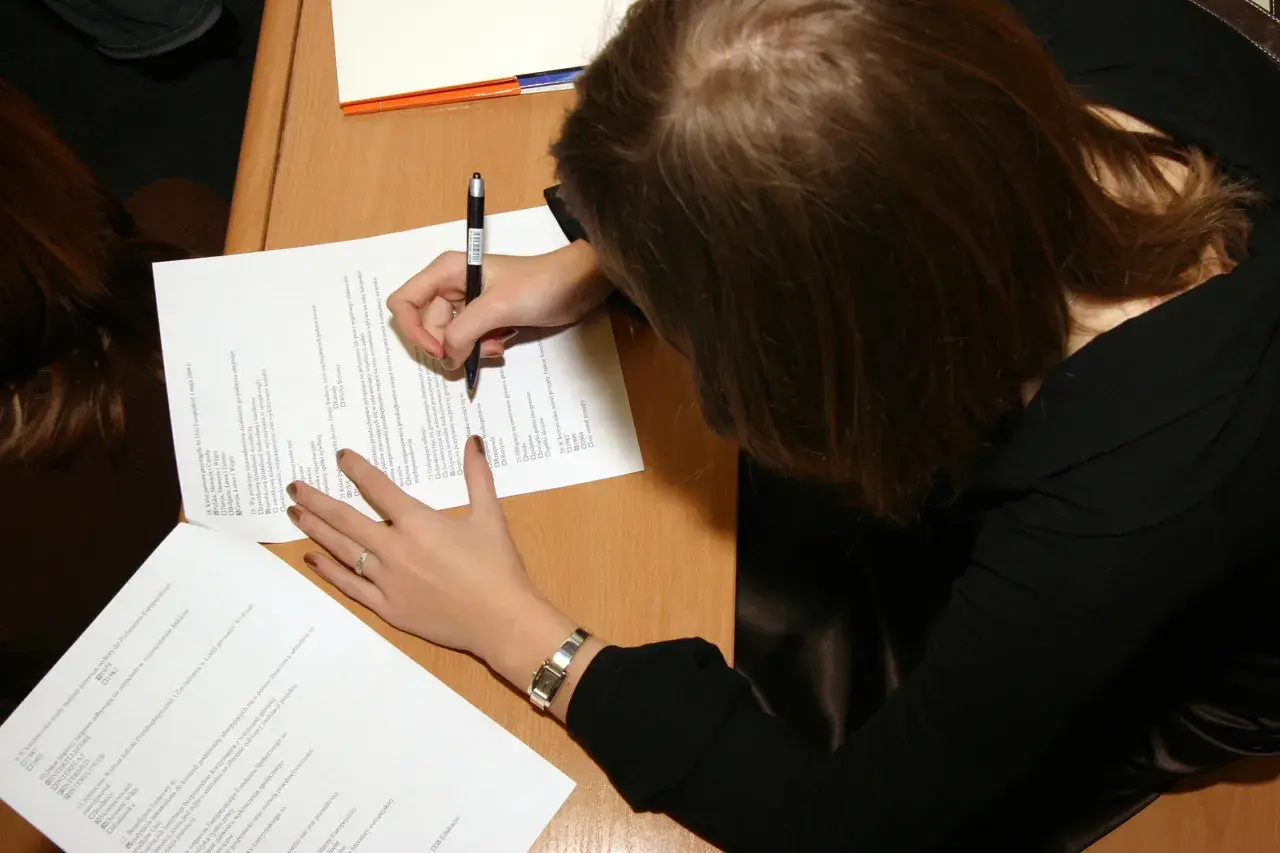 Kobieta pisze na kartce, ucząc się, jak zostać rzeczoznawcą majątkowym.