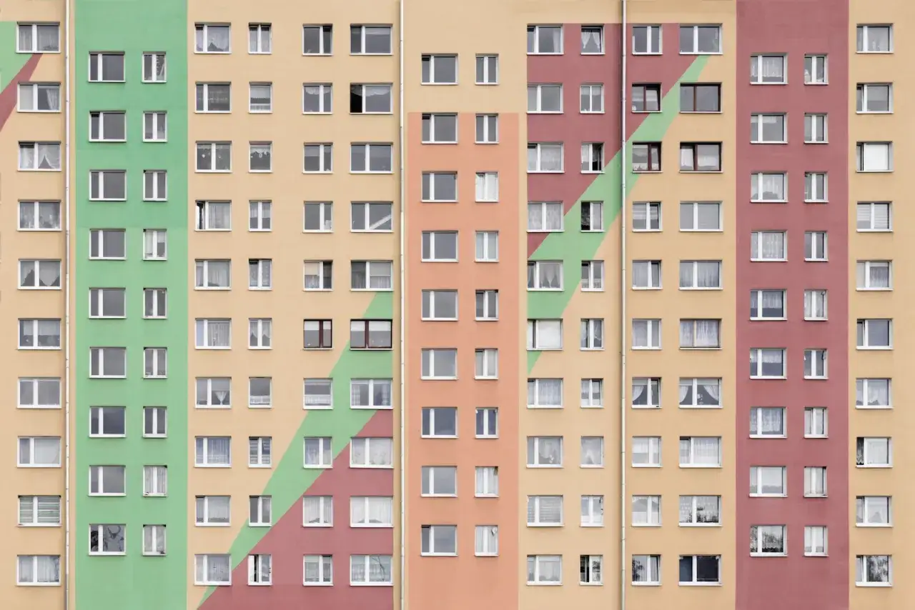 Wielopiętrowy blok mieszkalny z kolorowymi pasami. Każde mieszkanie ma spółdzielcze wł prawo do lokalu, widoczne przez liczne okna.