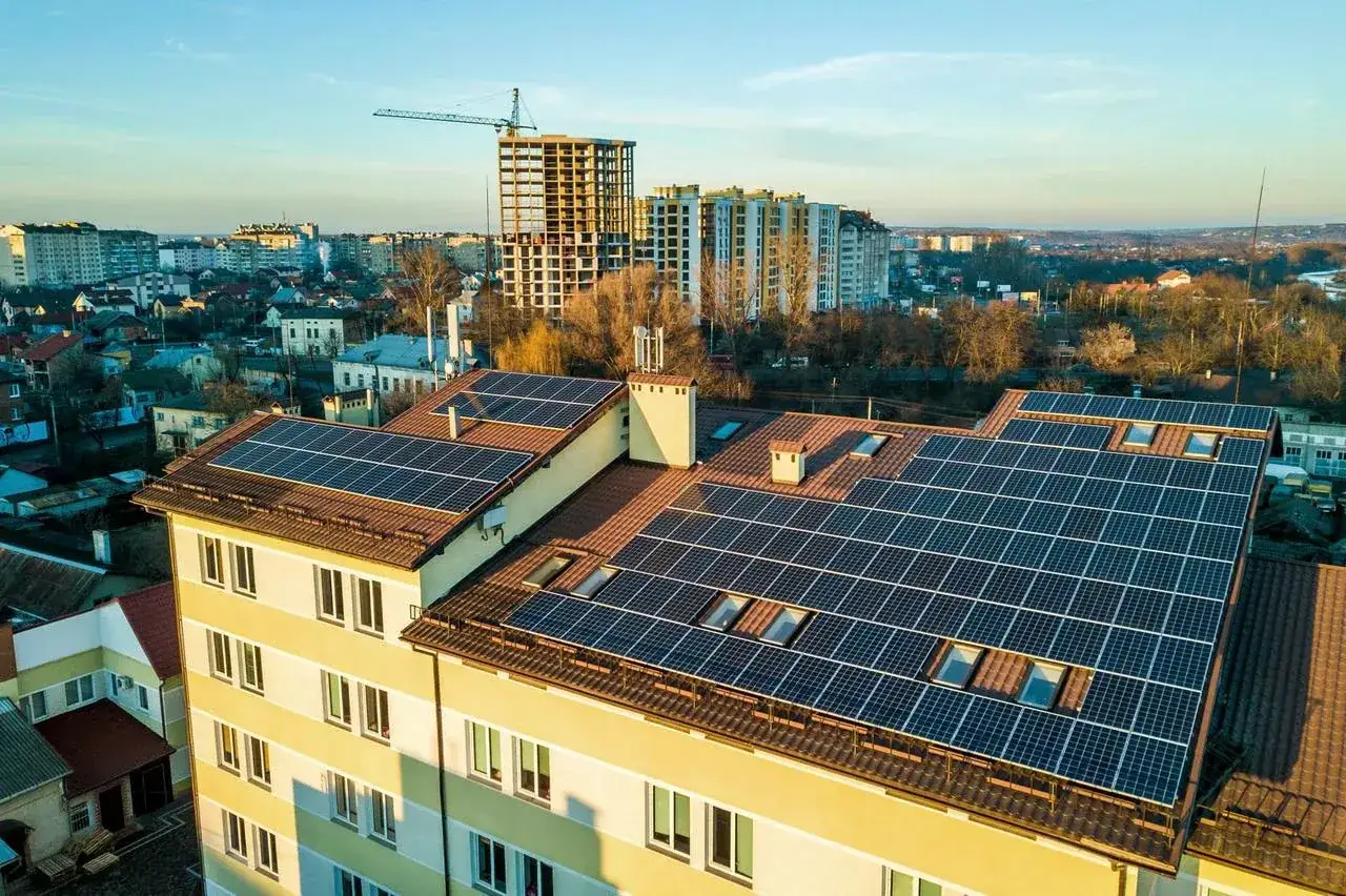 Dach budynku mieszkalnego pokryty panelami słonecznymi, świadczącymi o inwestycji w zieloną energię. Wspólnota mieszkaniowa skorzystała z kredytu na ekologiczne rozwiązania.