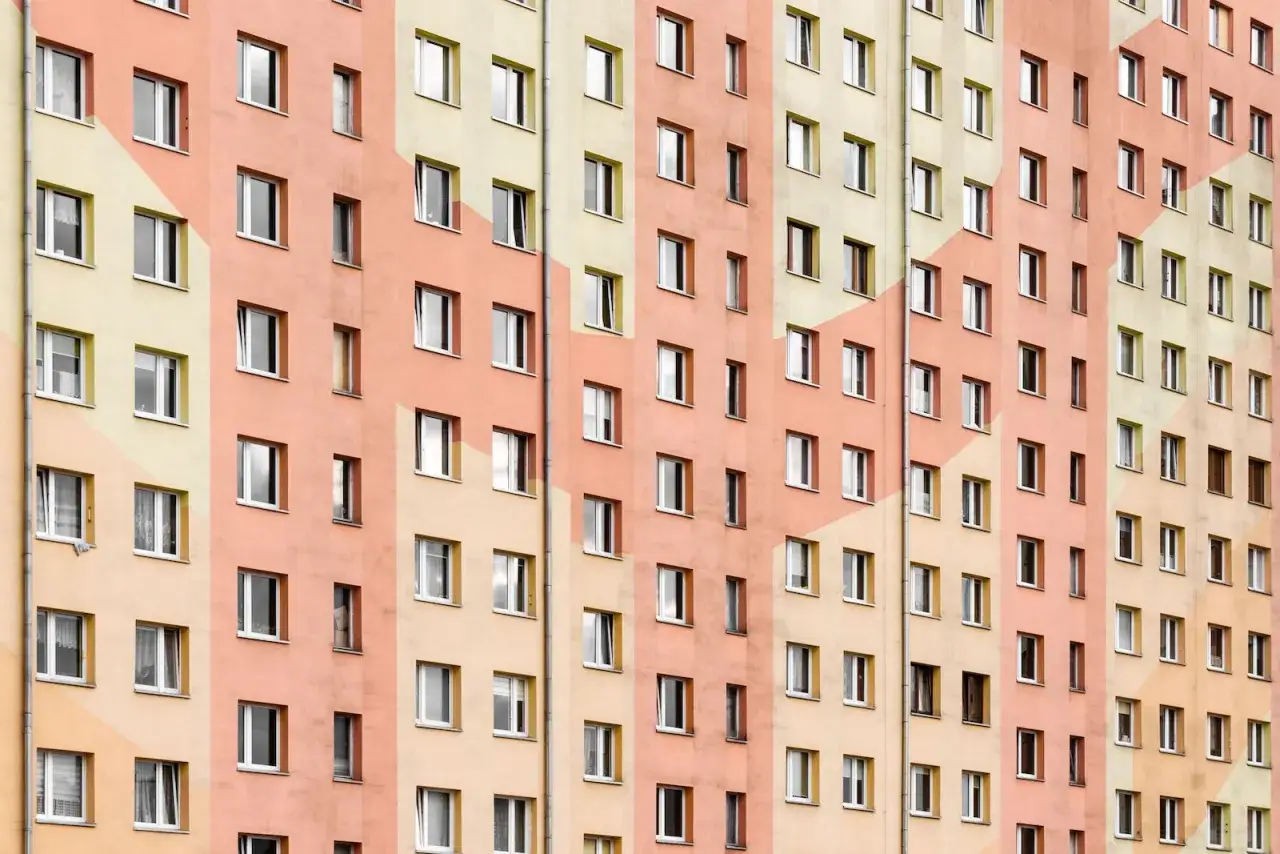 Wielopiętrowy blok mieszkalny w pastelowych kolorach. Wiele okien, każde z nich to potencjalne spółdzielcze wł prawo do lokalu.