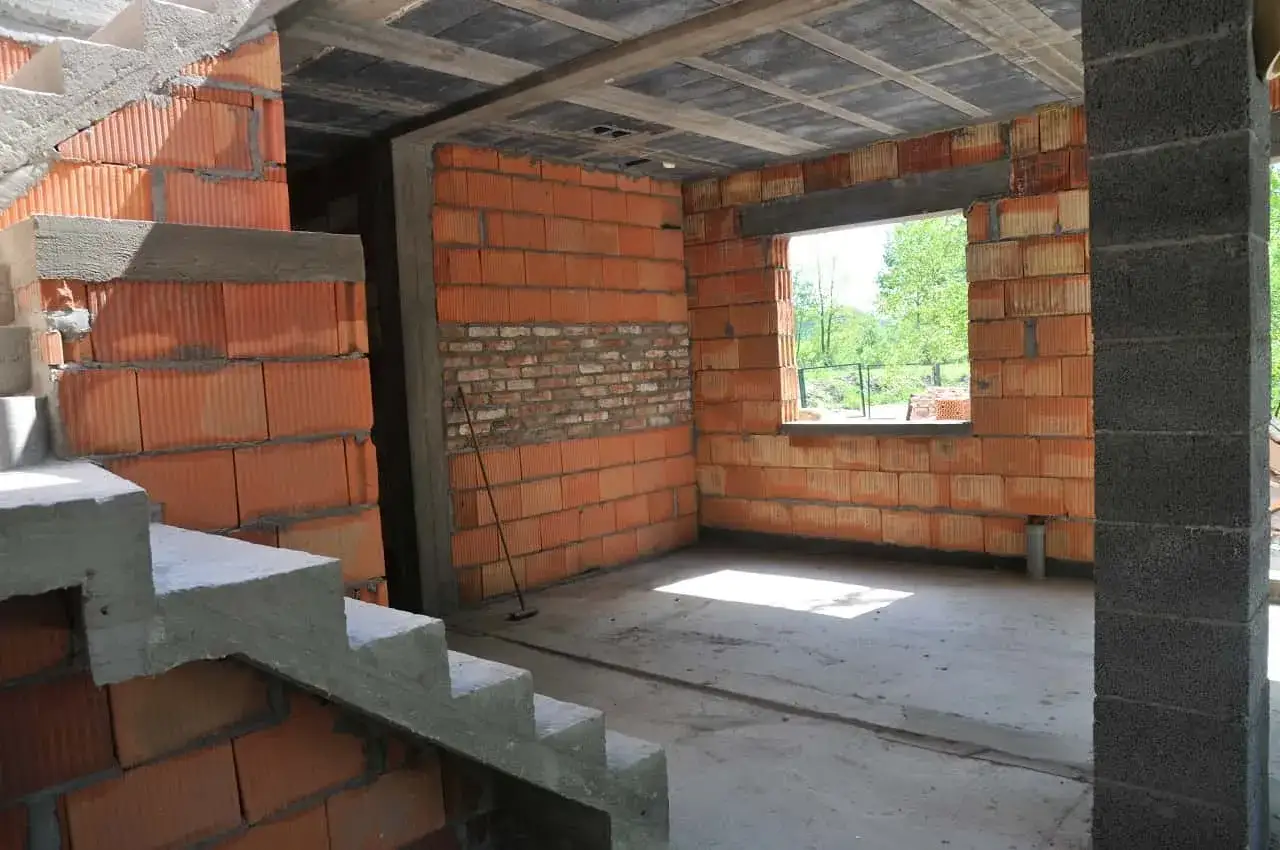 Budynek gospodarczy w trakcie adaptacji na cele mieszkalne. Widoczne schody, ściany z pustaków ceramicznych i betonowy słup.