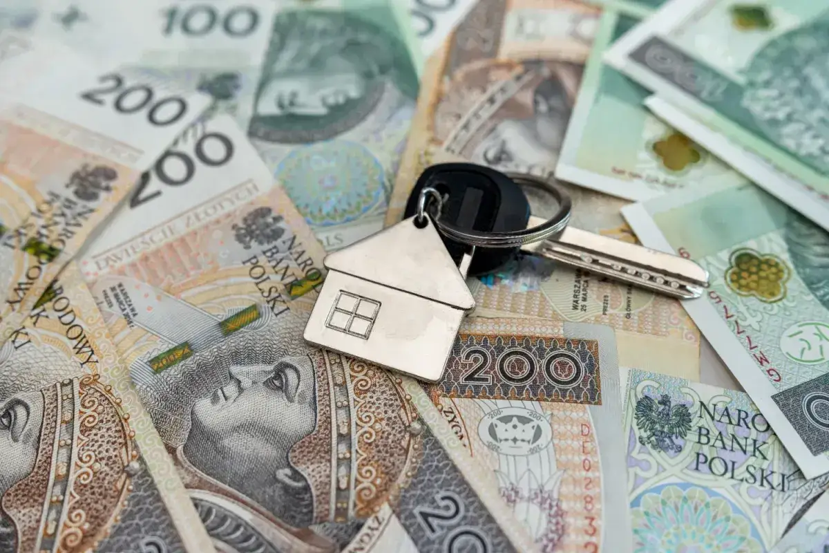 Klucze do domu na stosie polskich banknotów. Symboliczny obraz darowizny domu od rodziców.